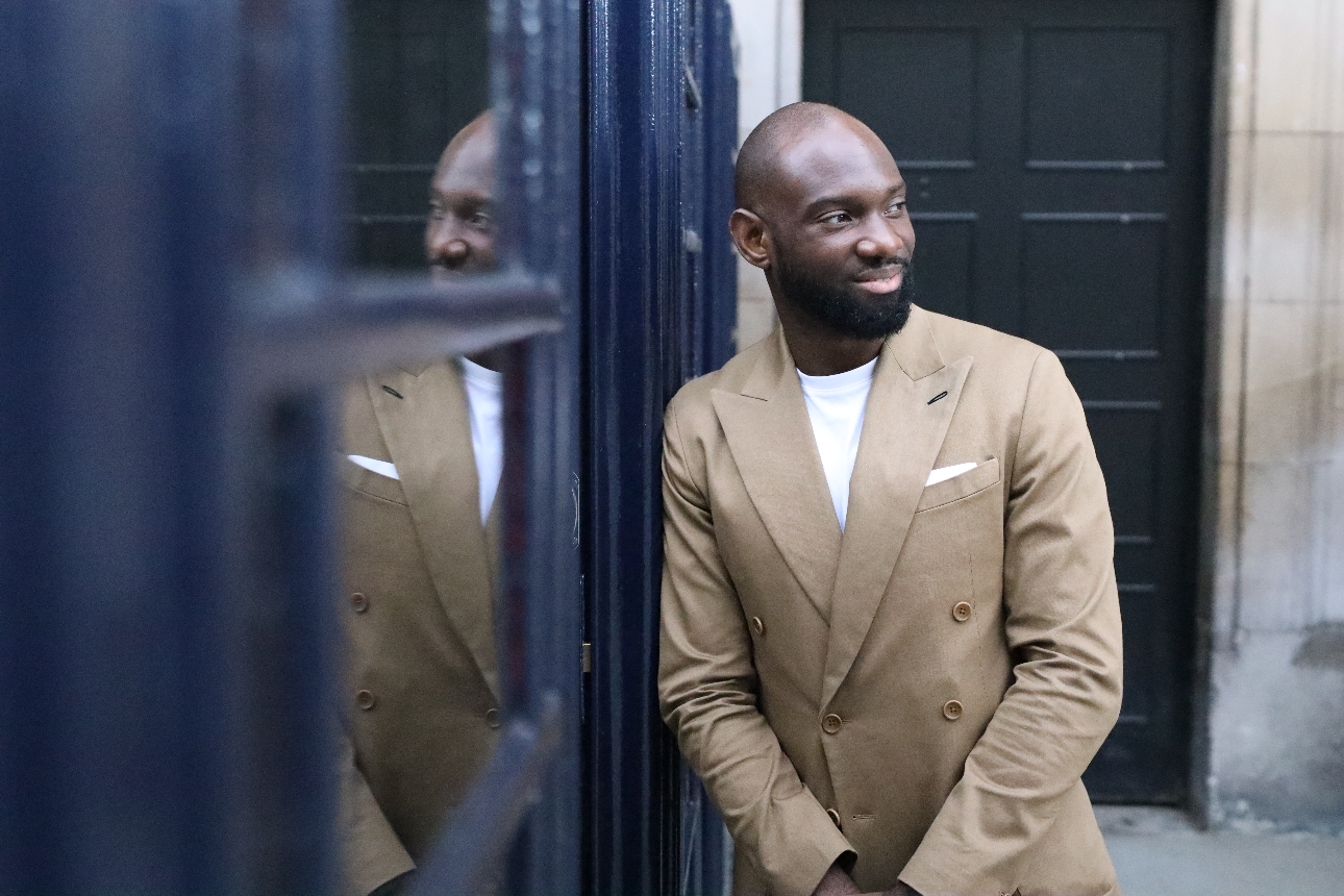 man in cream suit leaning on blue door